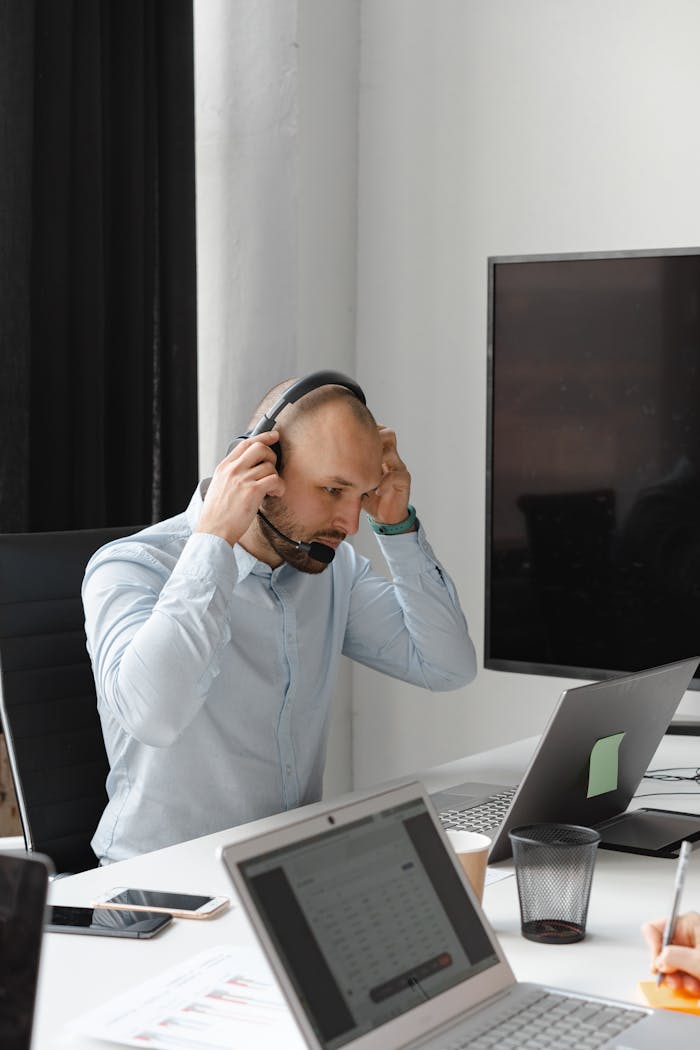 A bald male call center agent adjusting his headset during work in a modern office setting.